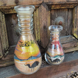 Two colored sand-art bottles depicting a desert scene with Jordan lettering.