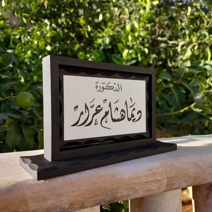 Rotating black wooden desk name sign with Arabic calligraphy on a white panel